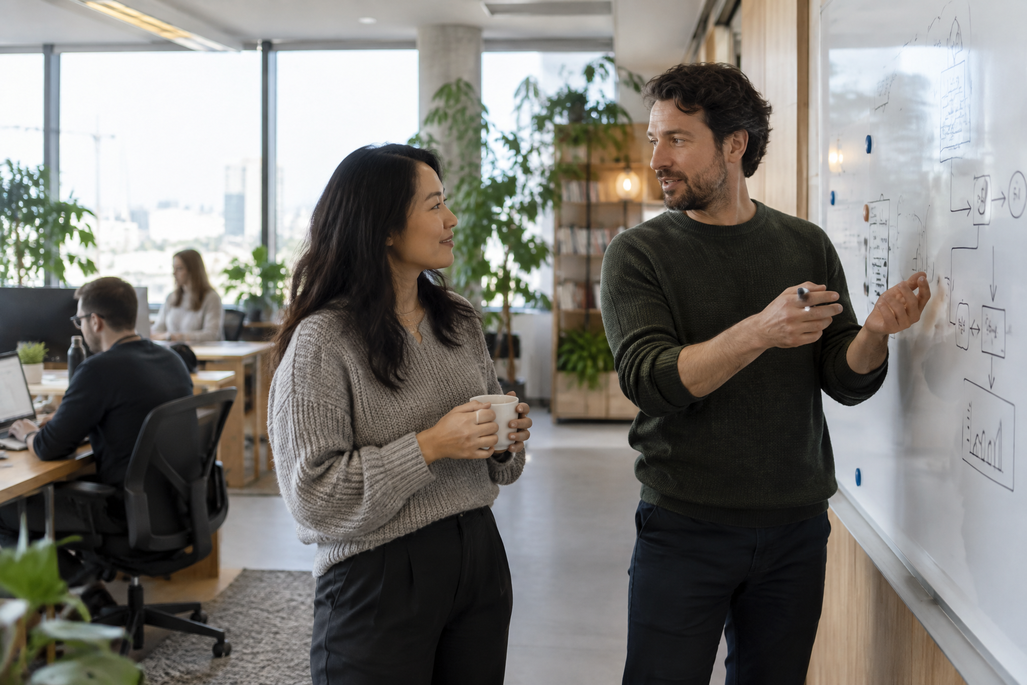 Two colleagues explaining a flow diagram at an office whiteboard